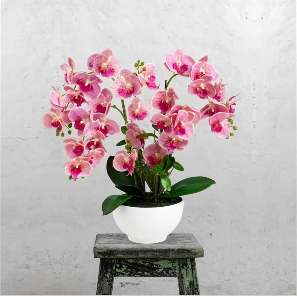 Top 10 plantas artificiales para 2026: orquídea rosa claro en maceta blanca sobre una silla de madera